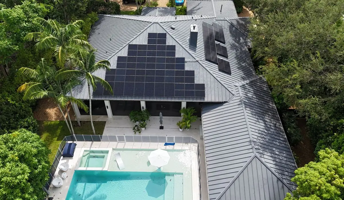Aerial drone view of a Florida home with rooftop solar panels on a metal roof, palm trees and a pool, installed by VOLT Home.