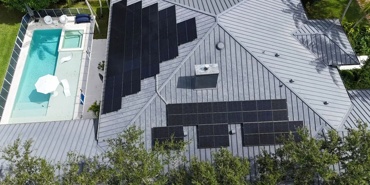 Aerial drone view of a Florida home with a metal roof, rooftop solar panels and a pool, installed by VOLT Home.